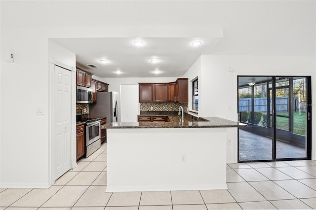 kitchen with backsplash, dark stone countertops, a peninsula, light tile patterned flooring, and stainless steel appliances