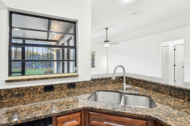 kitchen featuring brown cabinetry, dishwashing machine, dark stone countertops, and a sink