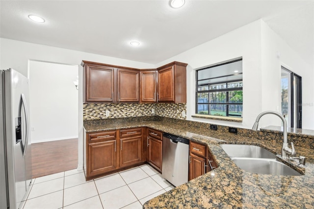 kitchen featuring a sink, dark stone countertops, tasteful backsplash, stainless steel appliances, and light tile patterned floors