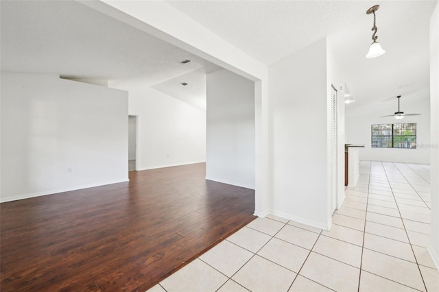 empty room with baseboards, light wood-style flooring, a ceiling fan, and vaulted ceiling