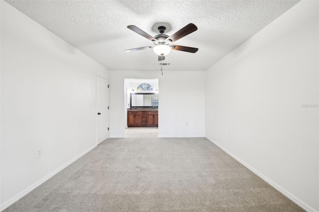 empty room featuring a ceiling fan, visible vents, baseboards, a textured ceiling, and light carpet