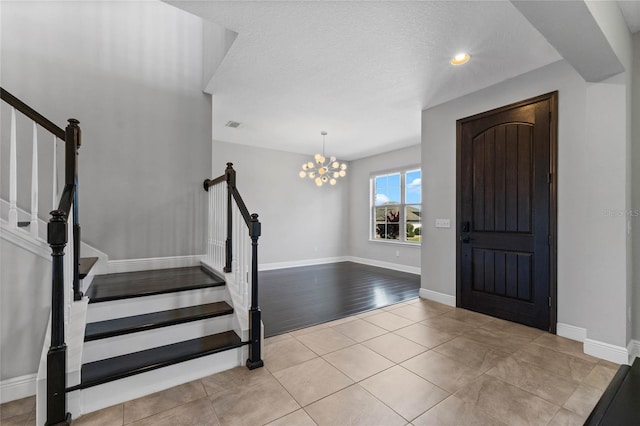 foyer with baseboards, an inviting chandelier, stairs, tile patterned flooring, and a textured ceiling