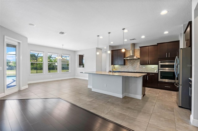 kitchen featuring visible vents, dark brown cabinets, wall chimney range hood, decorative backsplash, and freestanding refrigerator