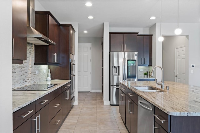 kitchen with a sink, stainless steel appliances, wall chimney exhaust hood, light stone countertops, and dark brown cabinets