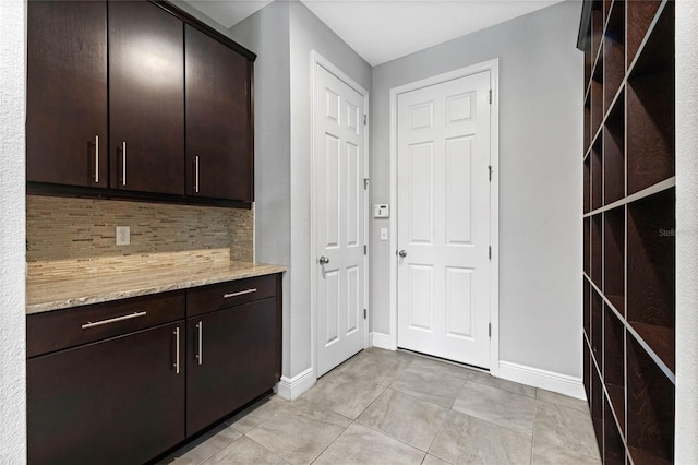 kitchen with light stone counters, light tile patterned floors, baseboards, dark brown cabinetry, and backsplash