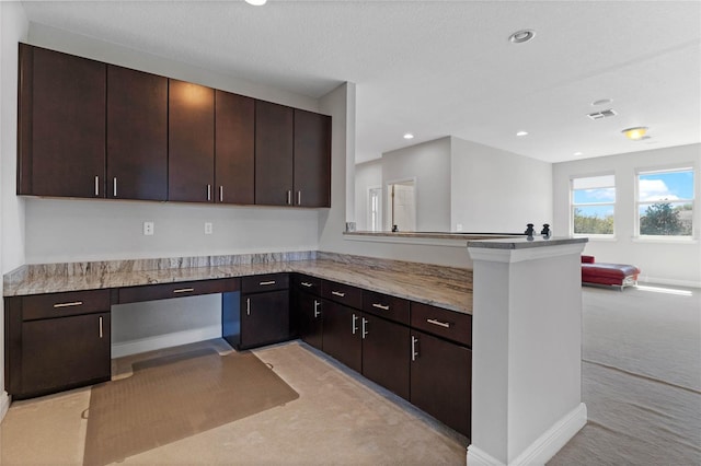 kitchen featuring visible vents, light carpet, built in desk, a peninsula, and dark brown cabinets