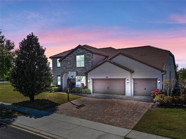 traditional-style house featuring stucco siding, decorative driveway, a front yard, a garage, and a tiled roof