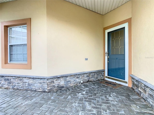 view of exterior entry with stucco siding, stone siding, and a patio area