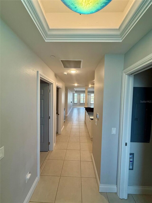 corridor featuring light tile patterned floors, attic access, a raised ceiling, and baseboards