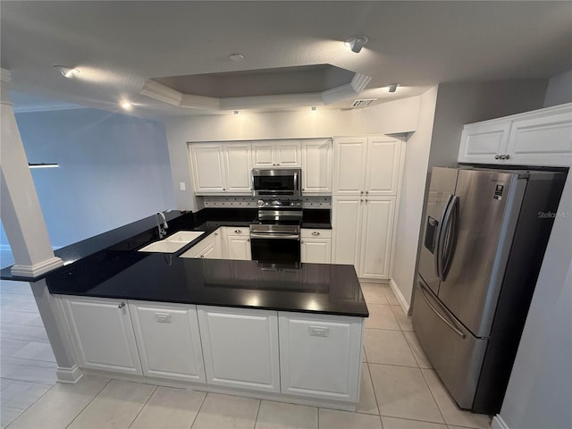 kitchen with a peninsula, a tray ceiling, a sink, appliances with stainless steel finishes, and dark countertops