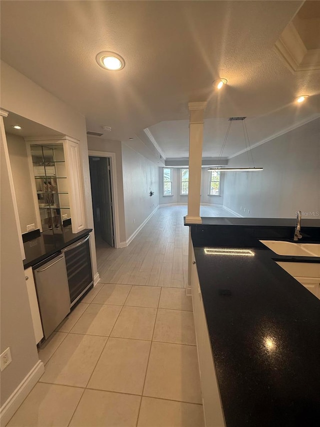 kitchen with a textured ceiling, decorative columns, light tile patterned floors, and a sink