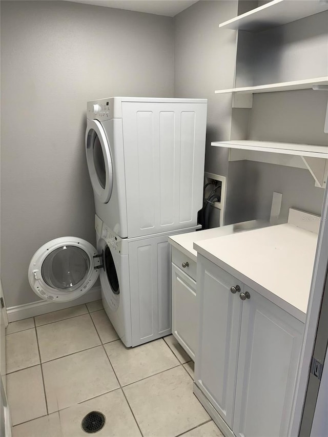 clothes washing area with light tile patterned flooring, cabinet space, and stacked washer and dryer