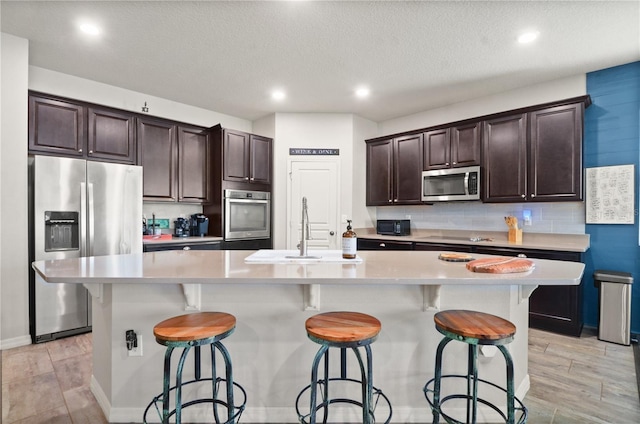 kitchen featuring stainless steel appliances, a spacious island, dark brown cabinets, and light countertops