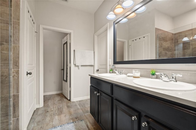 bathroom featuring double vanity, tiled shower, baseboards, and a sink