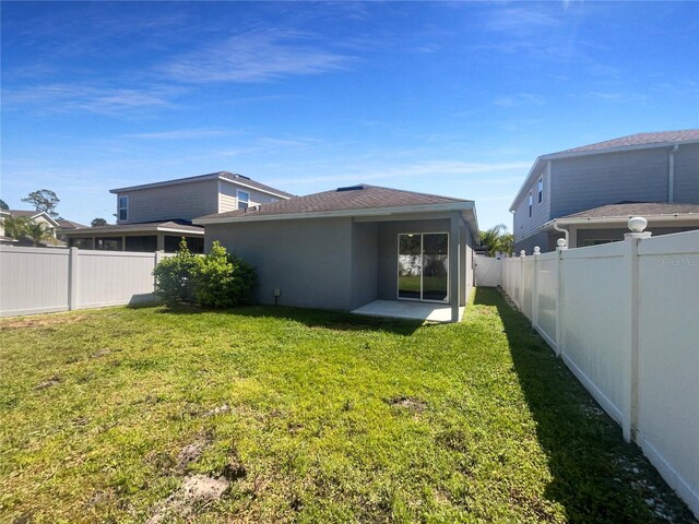 rear view of house with a fenced backyard, stucco siding, a yard, and roof with shingles