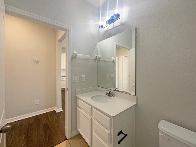 half bath featuring baseboards, toilet, wood finished floors, and vanity