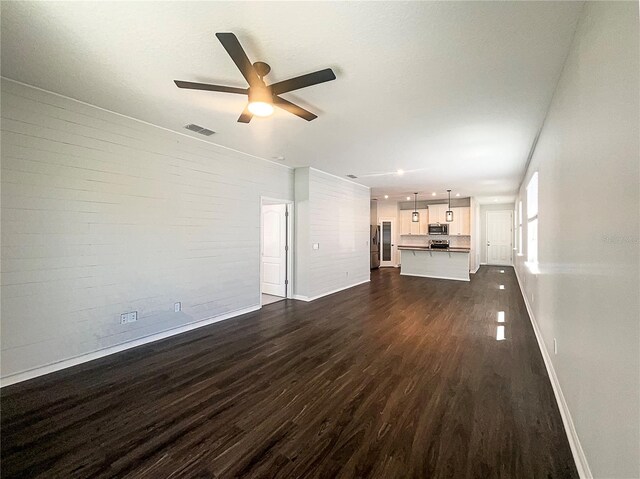 unfurnished living room featuring visible vents, dark wood finished floors, brick wall, baseboards, and ceiling fan