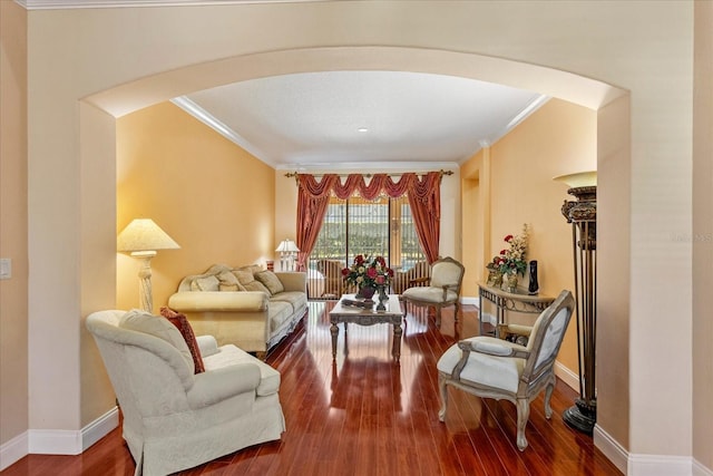 sitting room featuring baseboards, arched walkways, wood finished floors, and crown molding