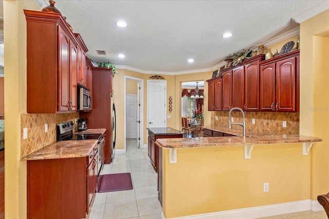 kitchen with a kitchen bar, light stone counters, appliances with stainless steel finishes, a peninsula, and reddish brown cabinets