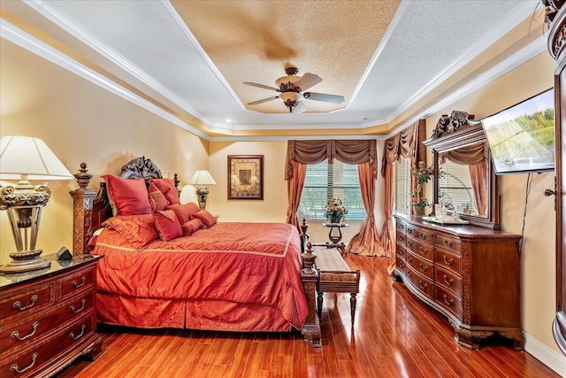 bedroom with ornamental molding, a textured ceiling, a tray ceiling, and wood finished floors