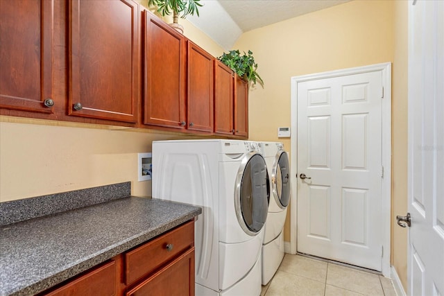 laundry area featuring a textured ceiling, light tile patterned flooring, cabinet space, and washing machine and clothes dryer