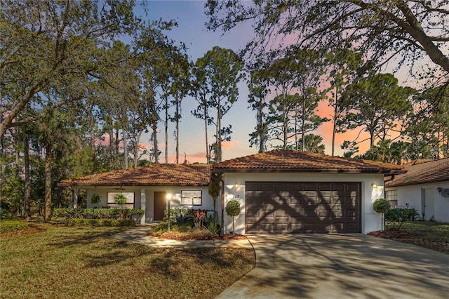 view of front facade with a front lawn, a tiled roof, concrete driveway, stucco siding, and a garage