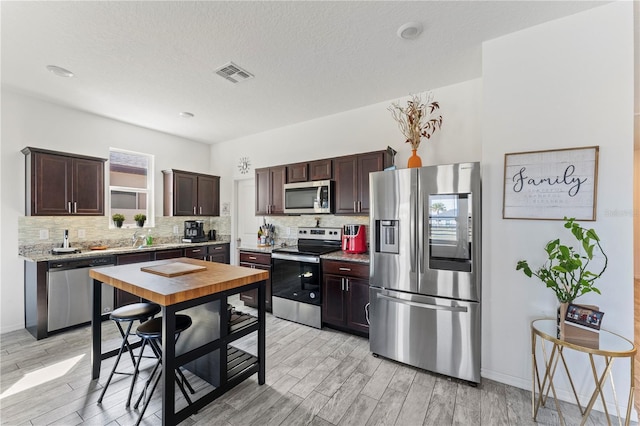 kitchen featuring visible vents, light wood-type flooring, tasteful backsplash, appliances with stainless steel finishes, and dark brown cabinets