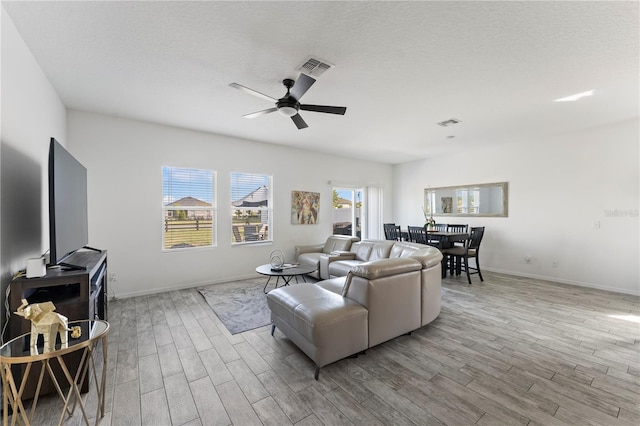 living room featuring wood finished floors, baseboards, visible vents, ceiling fan, and a textured ceiling