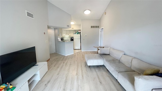 living area with visible vents, a towering ceiling, and light wood-type flooring