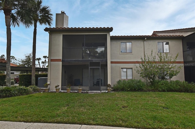 rear view of property with stucco siding, a yard, and a chimney