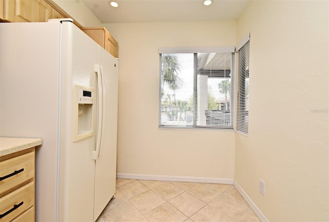 kitchen with baseboards, recessed lighting, light brown cabinetry, light countertops, and white refrigerator with ice dispenser