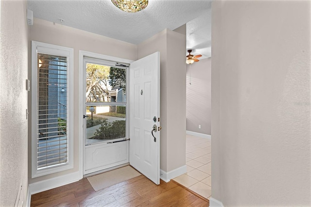 entrance foyer featuring ceiling fan, a textured ceiling, baseboards, and wood-type flooring