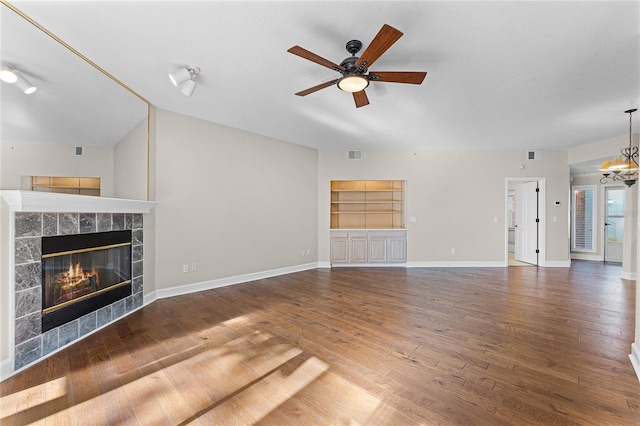 unfurnished living room with wood finished floors, baseboards, visible vents, a fireplace, and ceiling fan with notable chandelier