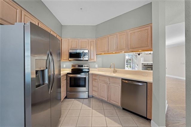 kitchen with light brown cabinetry, a sink, appliances with stainless steel finishes, light countertops, and light tile patterned floors