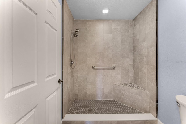 full bath featuring a textured ceiling, toilet, and tiled shower