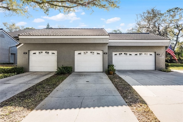 view of front of property with stucco siding, a tiled roof, driveway, and a garage