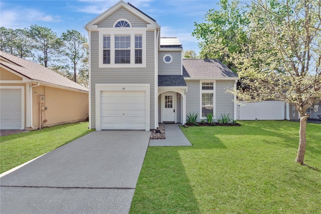 traditional-style house with a front yard, fence, roof with shingles, an attached garage, and concrete driveway