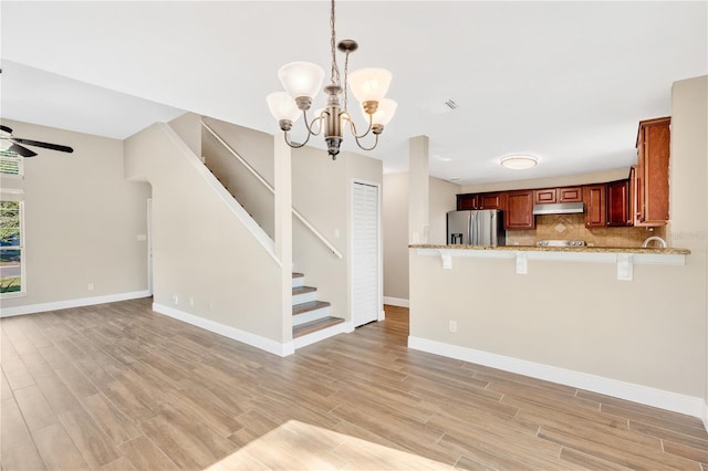 kitchen with light wood-type flooring, open floor plan, stainless steel fridge, a peninsula, and decorative backsplash