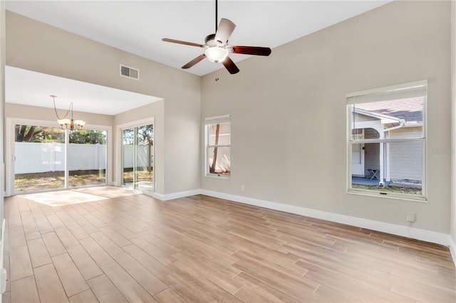 spare room with visible vents, light wood-style flooring, ceiling fan with notable chandelier, and baseboards