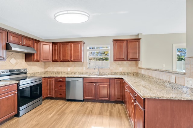 kitchen featuring light stone countertops, a peninsula, a sink, stainless steel appliances, and under cabinet range hood