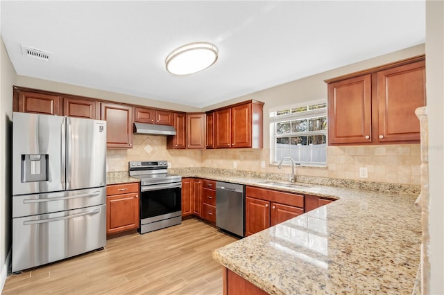 kitchen with under cabinet range hood, stainless steel appliances, light stone countertops, and a sink