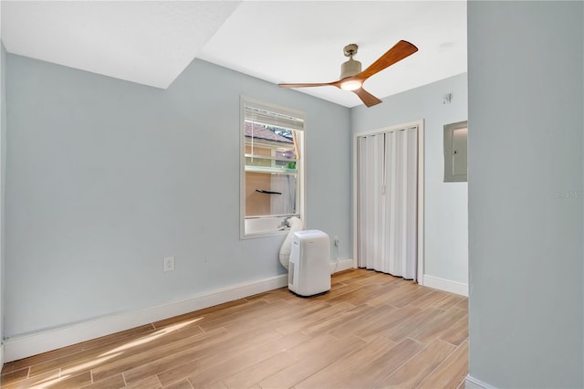 unfurnished bedroom featuring electric panel, baseboards, light wood-style flooring, and ceiling fan