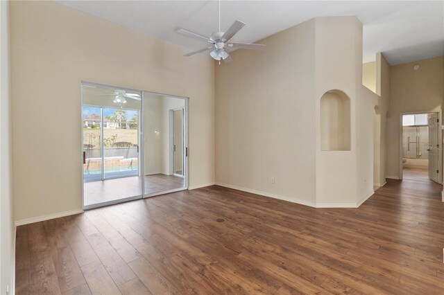 empty room with baseboards, a ceiling fan, a towering ceiling, and wood-type flooring