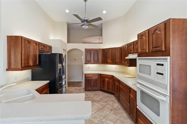 kitchen featuring a sink, under cabinet range hood, white appliances, light countertops, and a towering ceiling