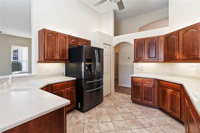 kitchen with ceiling fan, light countertops, black refrigerator with ice dispenser, arched walkways, and a sink