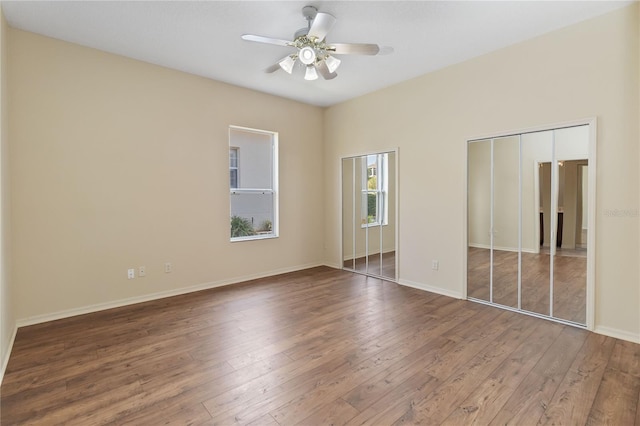 unfurnished bedroom with two closets, baseboards, and wood-type flooring