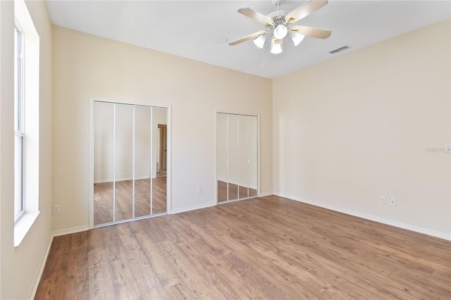 unfurnished bedroom featuring visible vents, two closets, baseboards, and wood finished floors