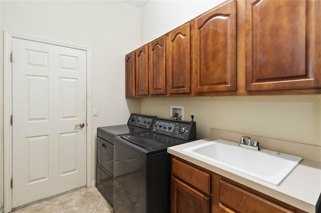 clothes washing area with cabinet space, light tile patterned floors, washer and dryer, and a sink