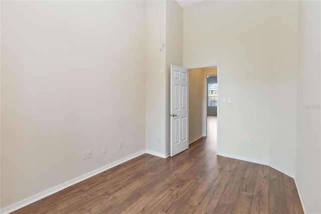 empty room with baseboards, wood finished floors, and a towering ceiling