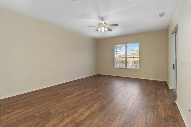 spare room featuring visible vents, dark wood-type flooring, a textured ceiling, baseboards, and ceiling fan